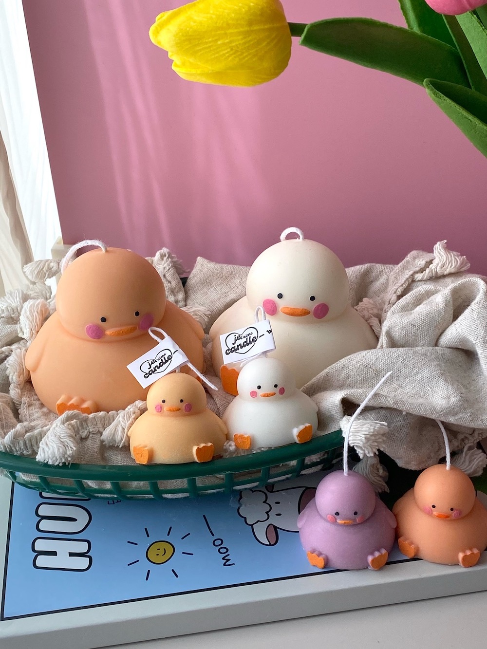 A close-up of four handcrafted duck-shaped candles in soft yellow tones with orange beaks and feet, and pink blushed cheeks, ideal for cute gifts or decorative accents. The candles are labeled with 'Je T’aime Candle' tags and are placed beside a dried floral arrangement, creating a soft, aesthetic backdrop. These adorable soy wax candles are perfect for baby showers, birthday favors, Easter gifts, or aesthetic room decor.