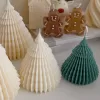Four tree-shaped candles in cream and green colors are displayed in the foreground, with house, reindeer, and gingerbread man candles in the background.