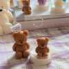 A collection of whimsical handmade bear-shaped candles in soft pastel colors, arranged on a cozy table. Each candle features intricate details. The candles are perfect for nursery decor, gifts, or home accents, adding warmth and charm to any space.