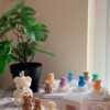 A collection of whimsical handmade bear-shaped candles in soft pastel colors, arranged on a cozy table. Each candle features intricate details. The candles are perfect for nursery decor, gifts, or home accents, adding warmth and charm to any space.