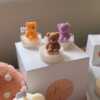A collection of whimsical handmade bear-shaped candles in soft pastel colors, arranged on a cozy table. Each candle features intricate details. The candles are perfect for nursery decor, gifts, or home accents, adding warmth and charm to any space.