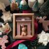 A cozy box featuring a teddy bear surrounded by festive Christmas decorations, perfect for holiday warmth and charm.