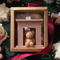 A cozy box featuring a teddy bear surrounded by festive Christmas decorations, perfect for holiday warmth and charm.