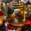 Two small bears on a table surrounded by festive Christmas decorations, one wearing a knitted hat and the other a scarf.