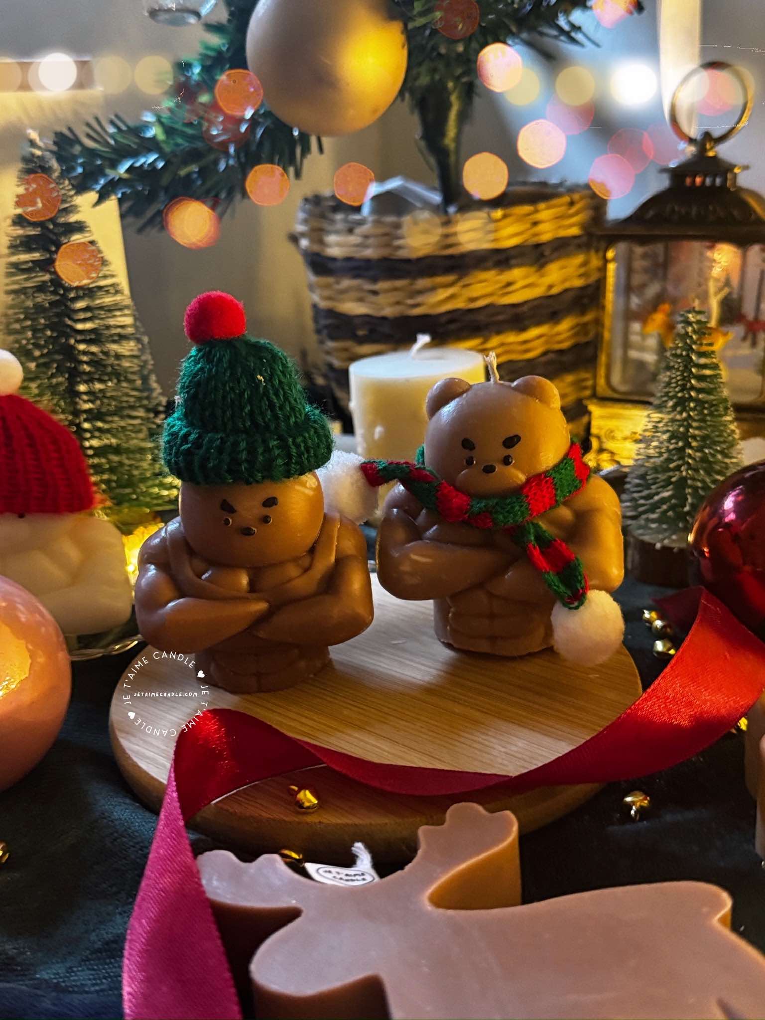 Two small bears on a table surrounded by festive Christmas decorations, one wearing a knitted hat and the other a scarf.