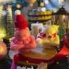 Two small bears on a table surrounded by festive Christmas decorations, one wearing a knitted hat and the other a scarf.