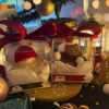 Two small bears on a table surrounded by festive Christmas decorations, one wearing a knitted hat and the other a scarf.