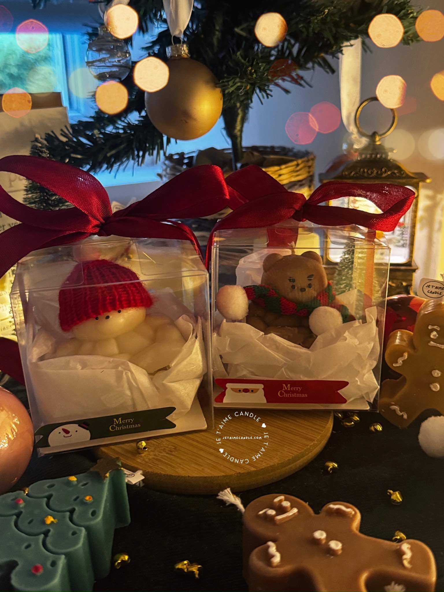 Two small bears on a table surrounded by festive Christmas decorations, one wearing a knitted hat and the other a scarf.