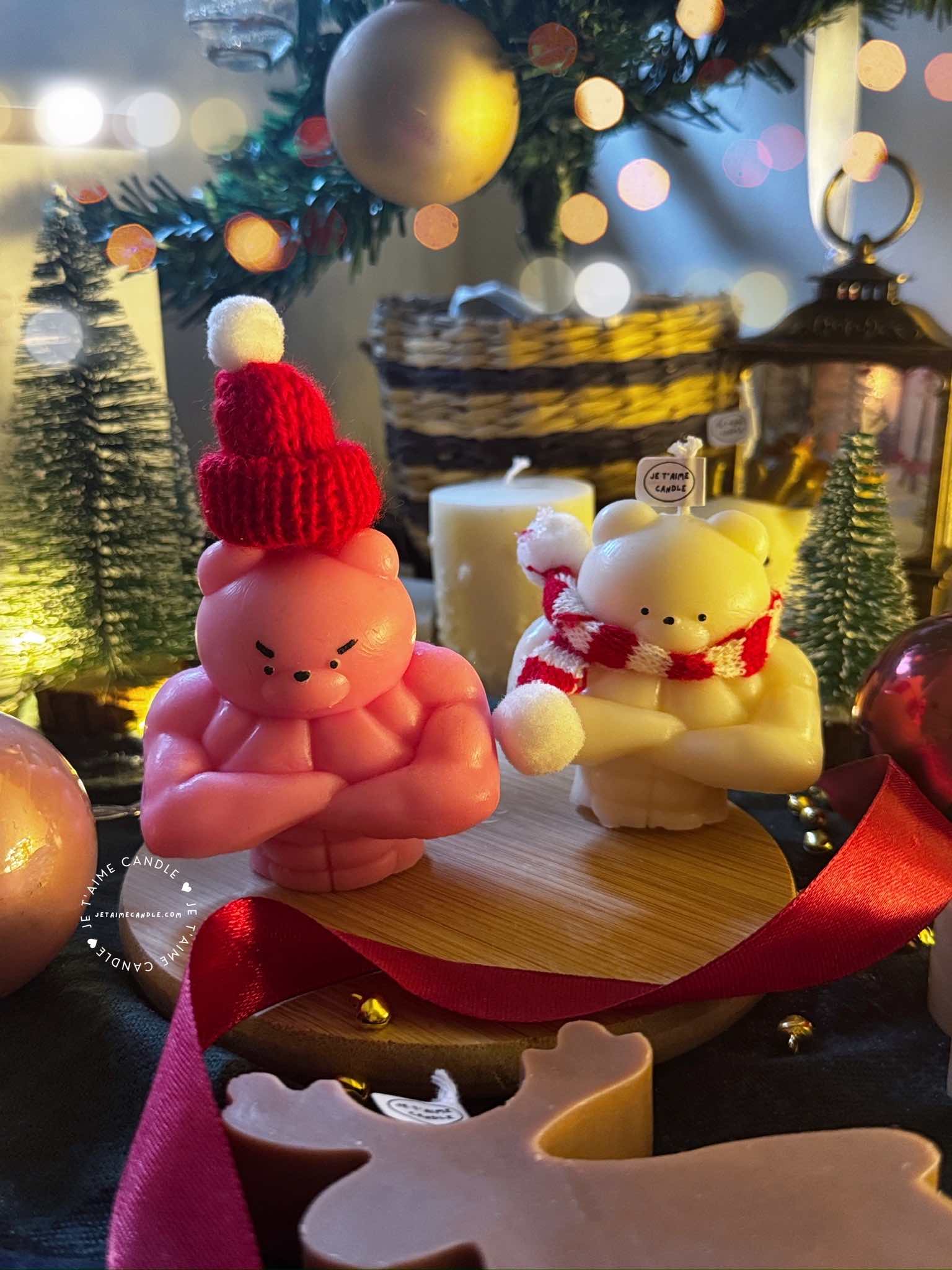 Two small bears on a table surrounded by festive Christmas decorations, one wearing a knitted hat and the other a scarf.