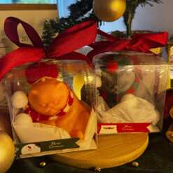 Two delightful toys in holiday-themed boxes, featuring Christmas decorations, including a Grumpy Cat Candle with a cozy hat.