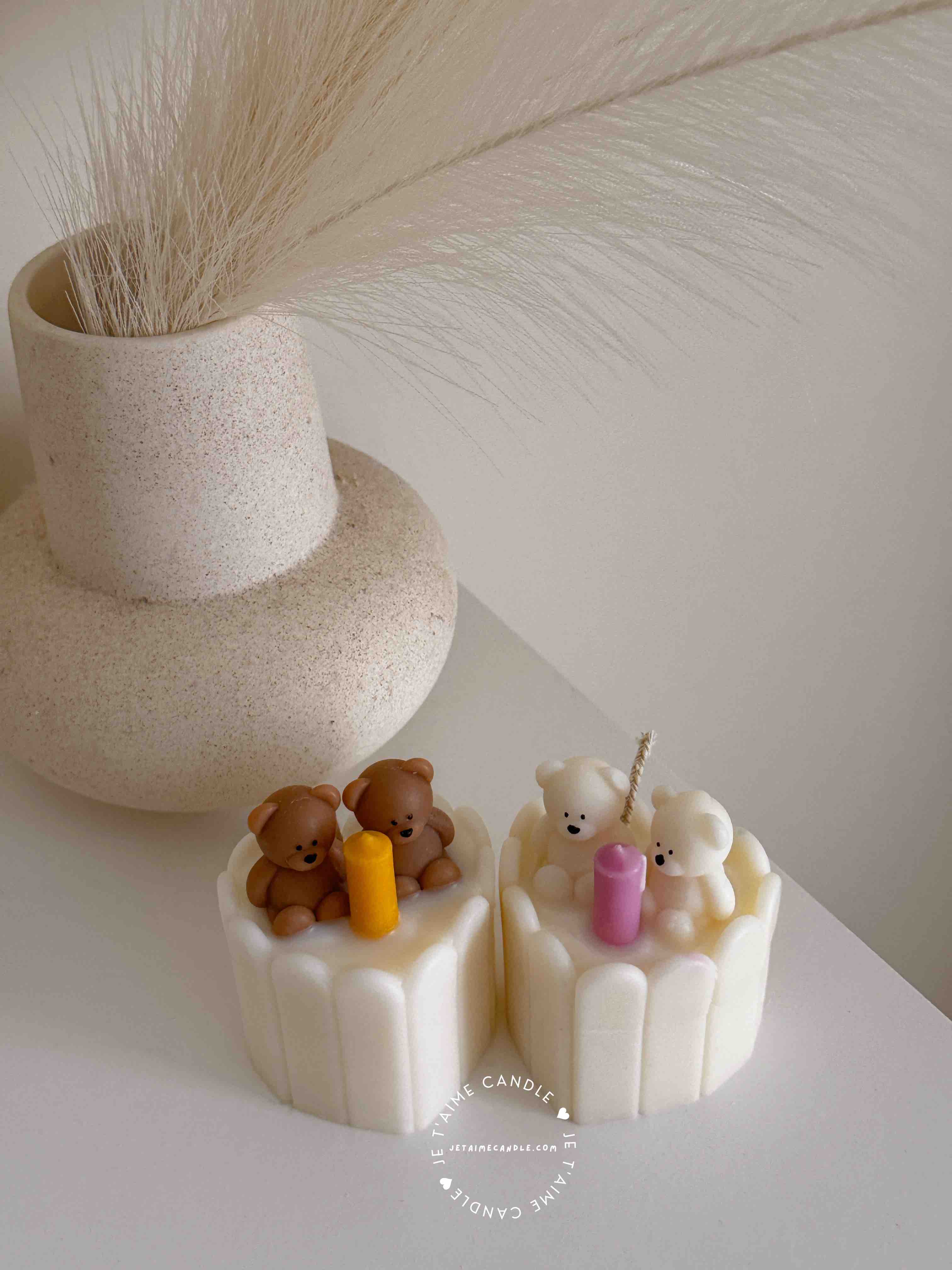 Two small cream white cakes topped with cute baby bear decorations and a colorful birthday candle.