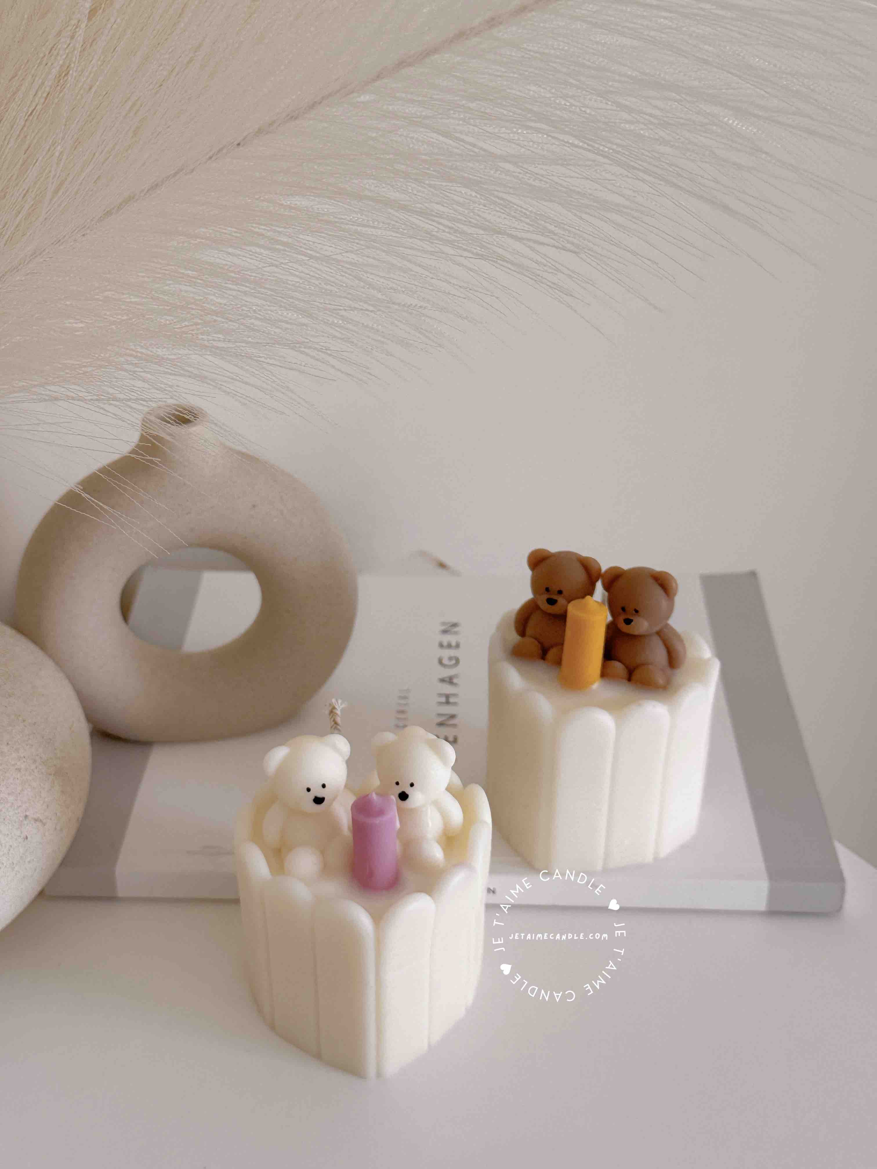Two small cream white cakes topped with cute baby bear decorations and a colorful birthday candle.