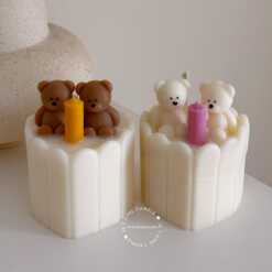 Two small cream white cakes topped with cute baby bear decorations and a colorful birthday candle.