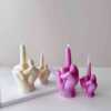 A row of multicolored candles shaped like hands making a gesture, lined up against a plain backdrop.