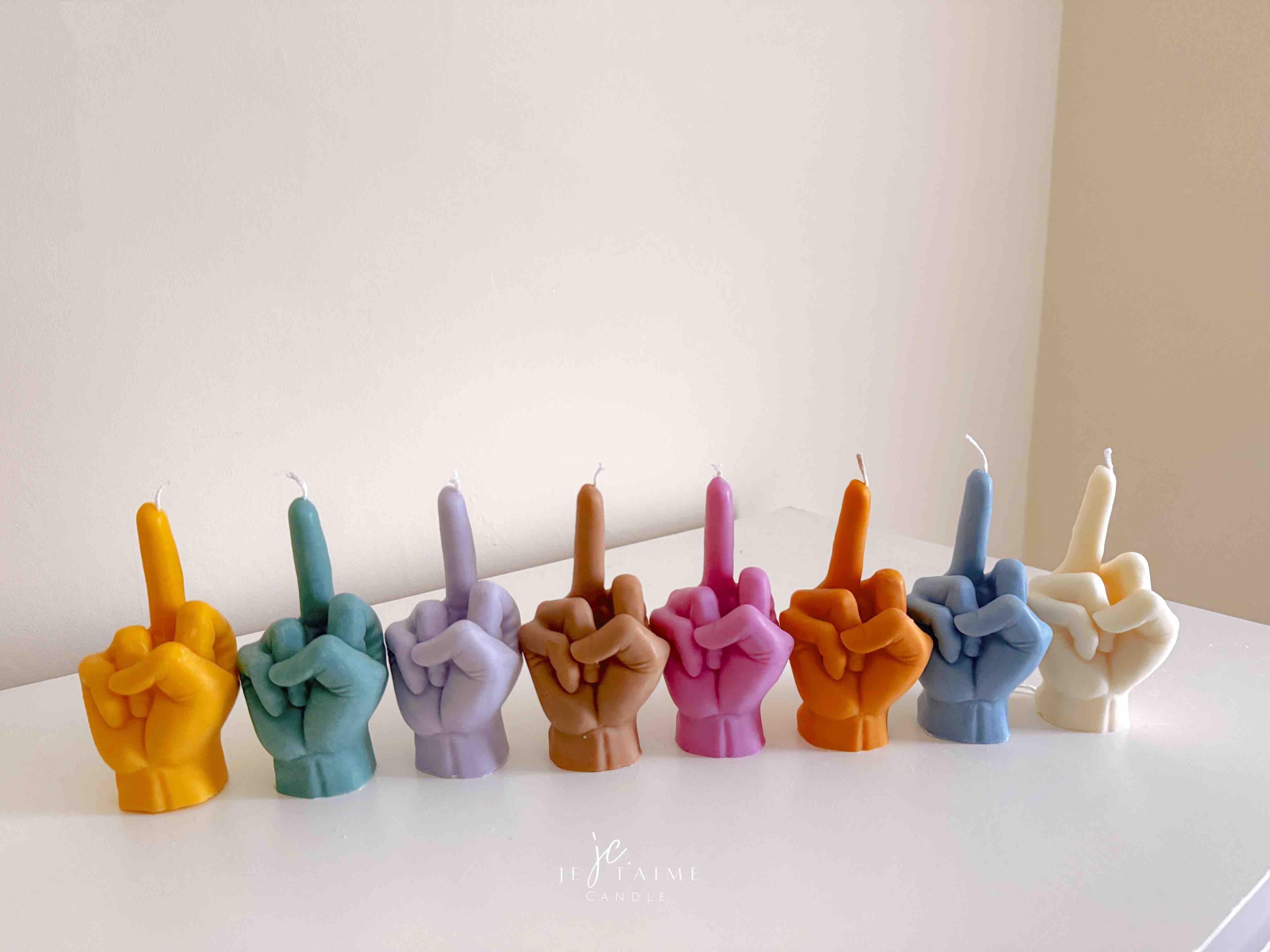 A row of multicolored candles shaped like hands making a gesture, lined up against a plain backdrop.