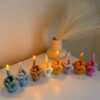 A row of multicolored candles shaped like hands making a gesture, lined up against a plain backdrop.