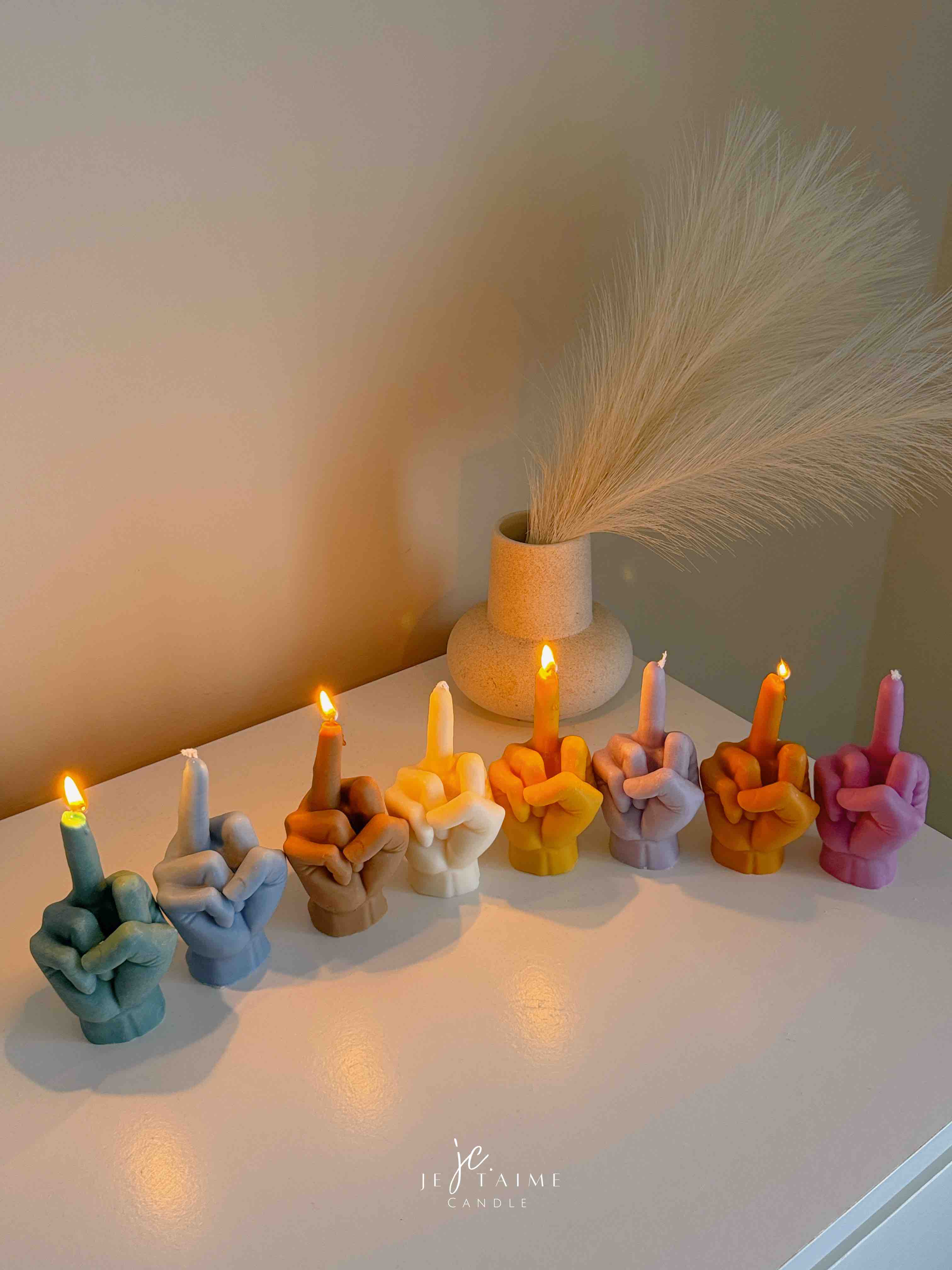 A row of multicolored candles shaped like hands making a gesture, lined up against a plain backdrop.