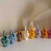 A row of multicolored candles shaped like hands making a gesture, lined up against a plain backdrop.