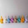 A row of multicolored candles shaped like hands making a gesture, lined up against a plain backdrop.
