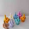 A row of multicolored candles shaped like hands making a gesture, lined up against a plain backdrop.