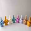 A row of multicolored candles shaped like hands making a gesture, lined up against a plain backdrop.