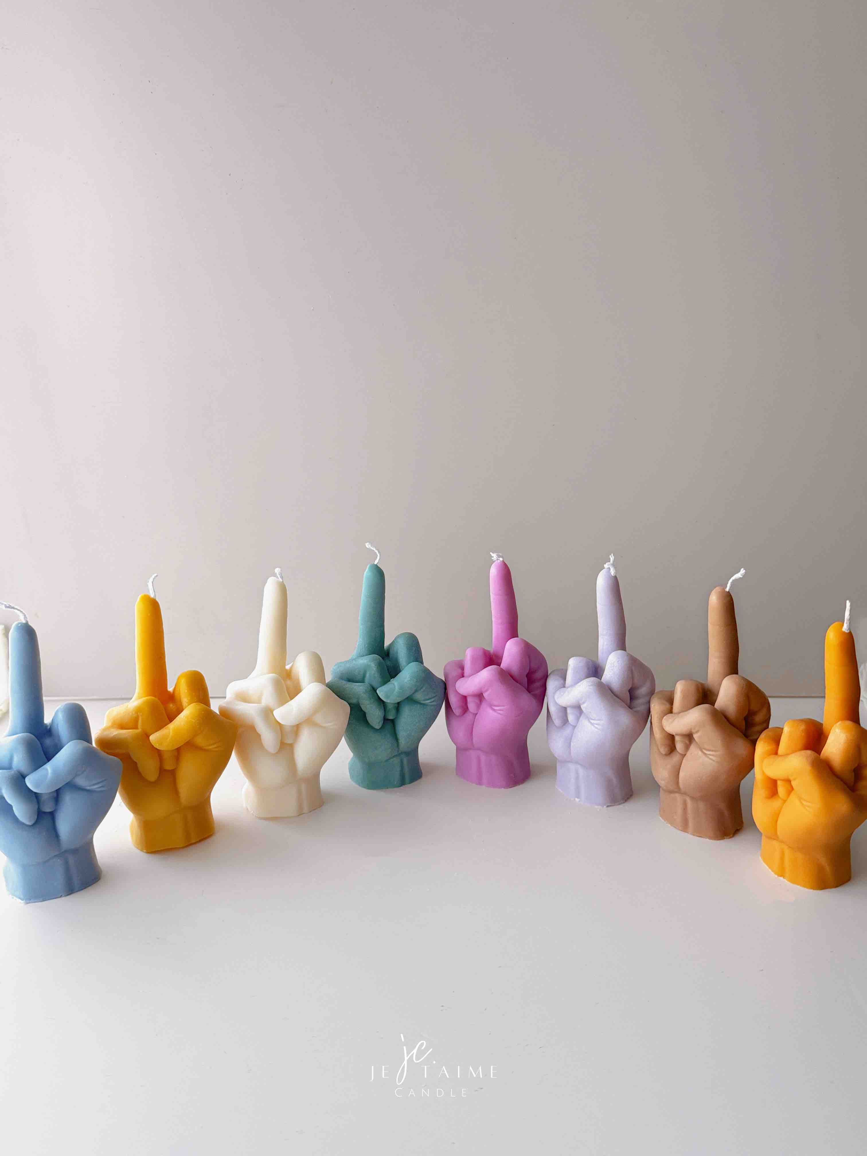 A row of multicolored candles shaped like hands making a gesture, lined up against a plain backdrop.