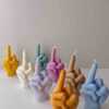 A row of multicolored candles shaped like hands making a gesture, lined up against a plain backdrop.