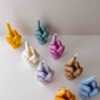 A row of multicolored candles shaped like hands making a gesture, lined up against a plain backdrop.