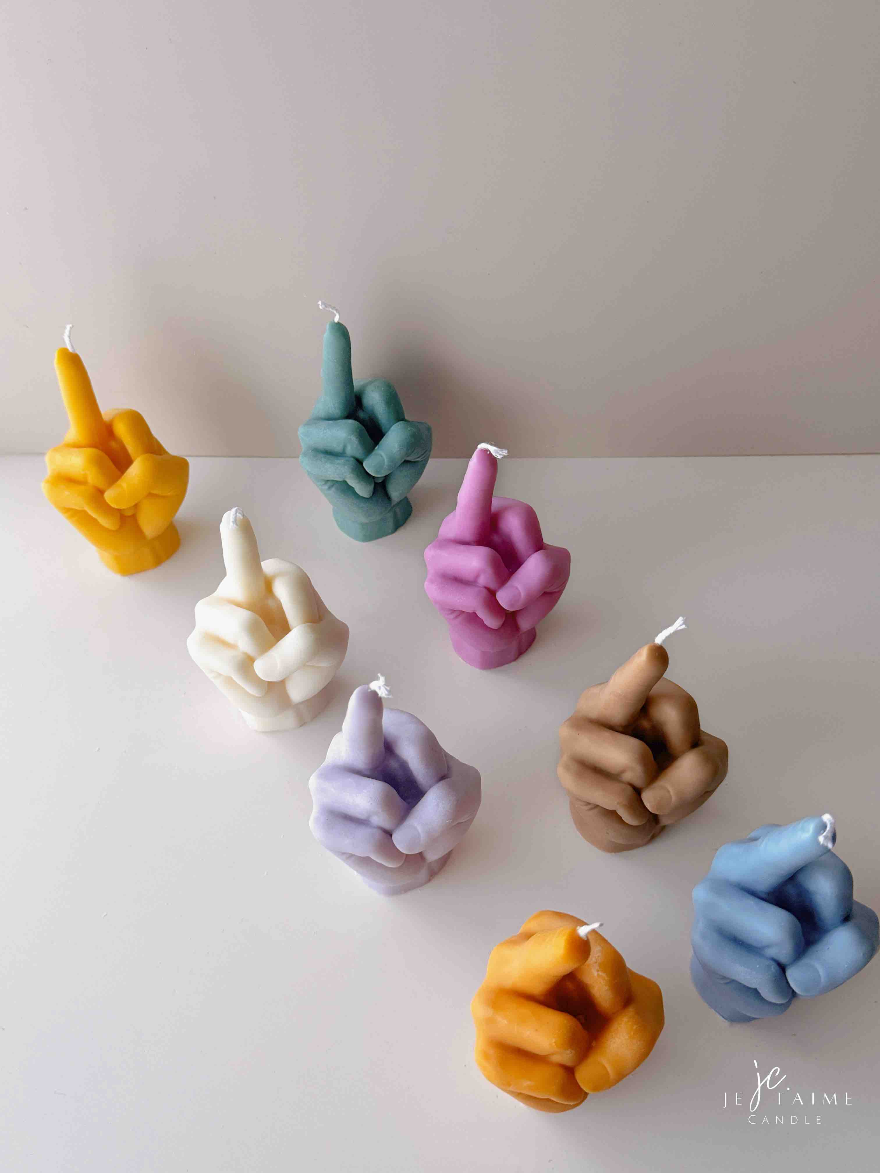 A row of multicolored candles shaped like hands making a gesture, lined up against a plain backdrop.