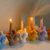A row of multicolored candles shaped like hands making a gesture, lined up against a plain backdrop.