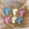 This image showcases beautifully packaged baby shower favors in the shape of small baby feet, made of wax. The favors come in pastel colors, including pink, blue, and white, and are individually wrapped in clear plastic with a 