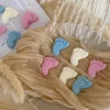 This image showcases beautifully packaged baby shower favors in the shape of small baby feet, made of wax. The favors come in pastel colors, including pink, blue, and white, and are individually wrapped in clear plastic with a 