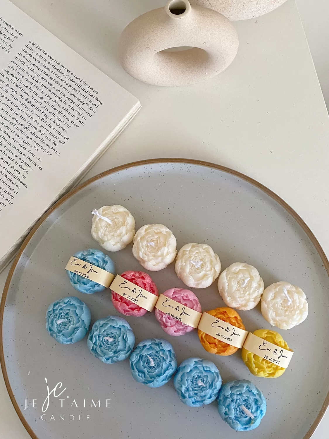 A book with an assortment of colorful candles on it, highlighting a Mini Peony Bud Candle, perfect for gifting at special events.