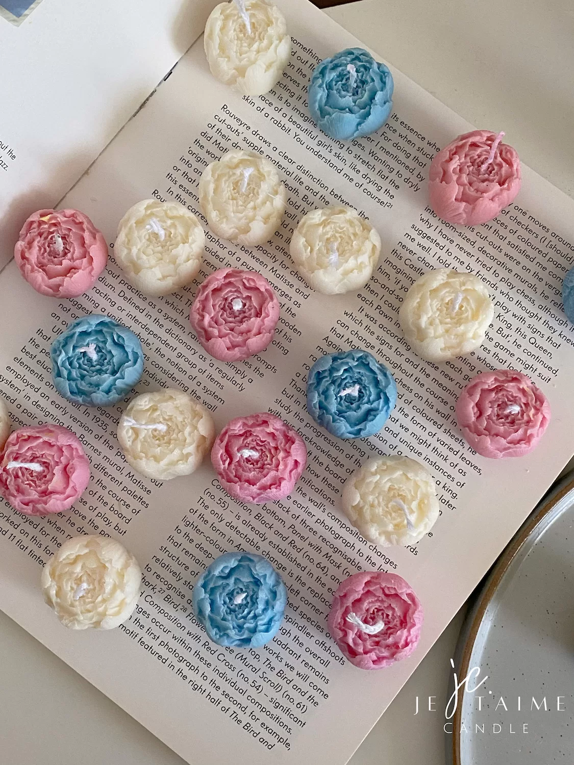 A book with an assortment of colorful candles on it, highlighting a Mini Peony Bud Candle, perfect for gifting at special events.