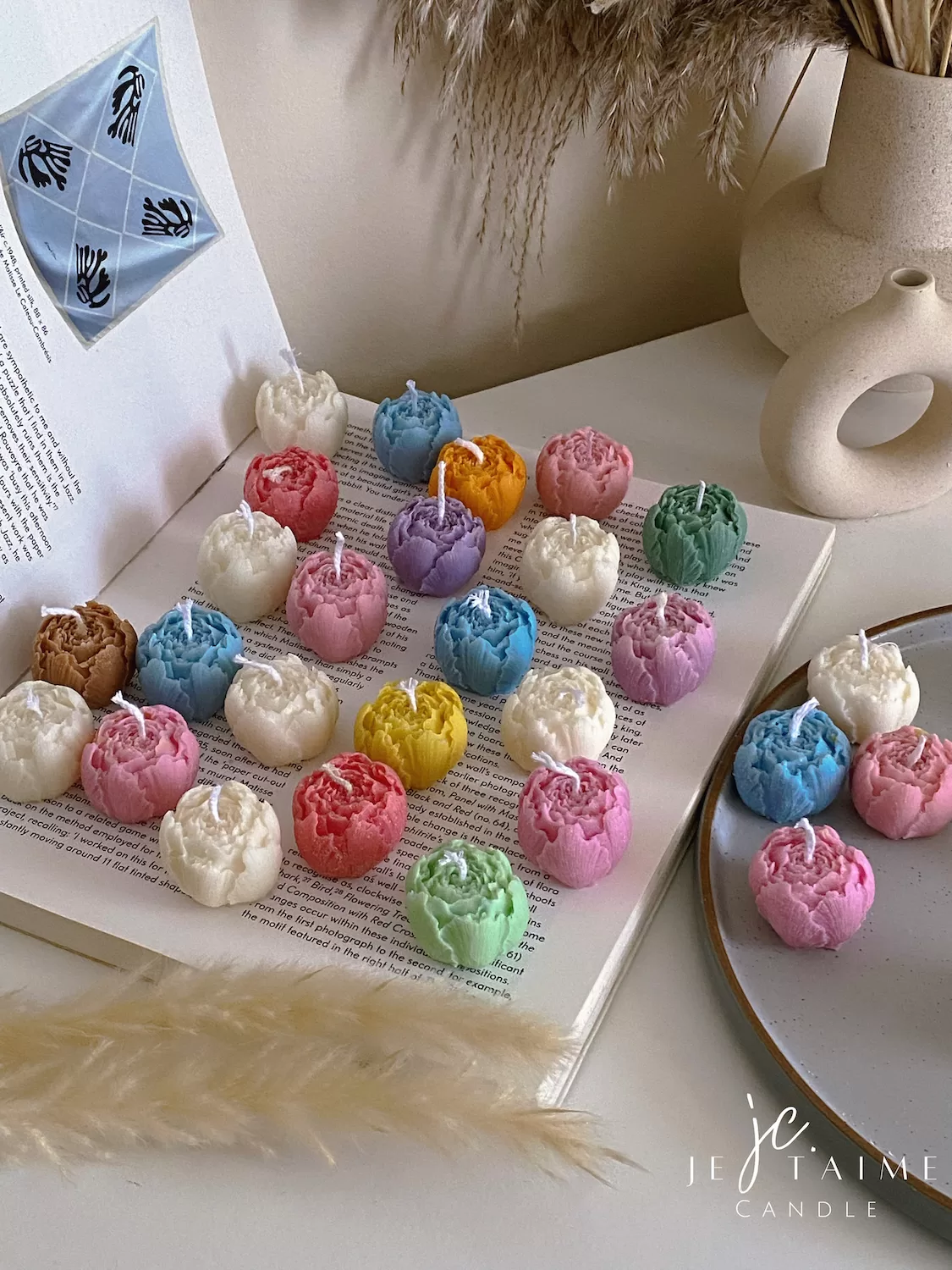A book with an assortment of colorful candles on it, highlighting a Mini Peony Bud Candle, perfect for gifting at special events.