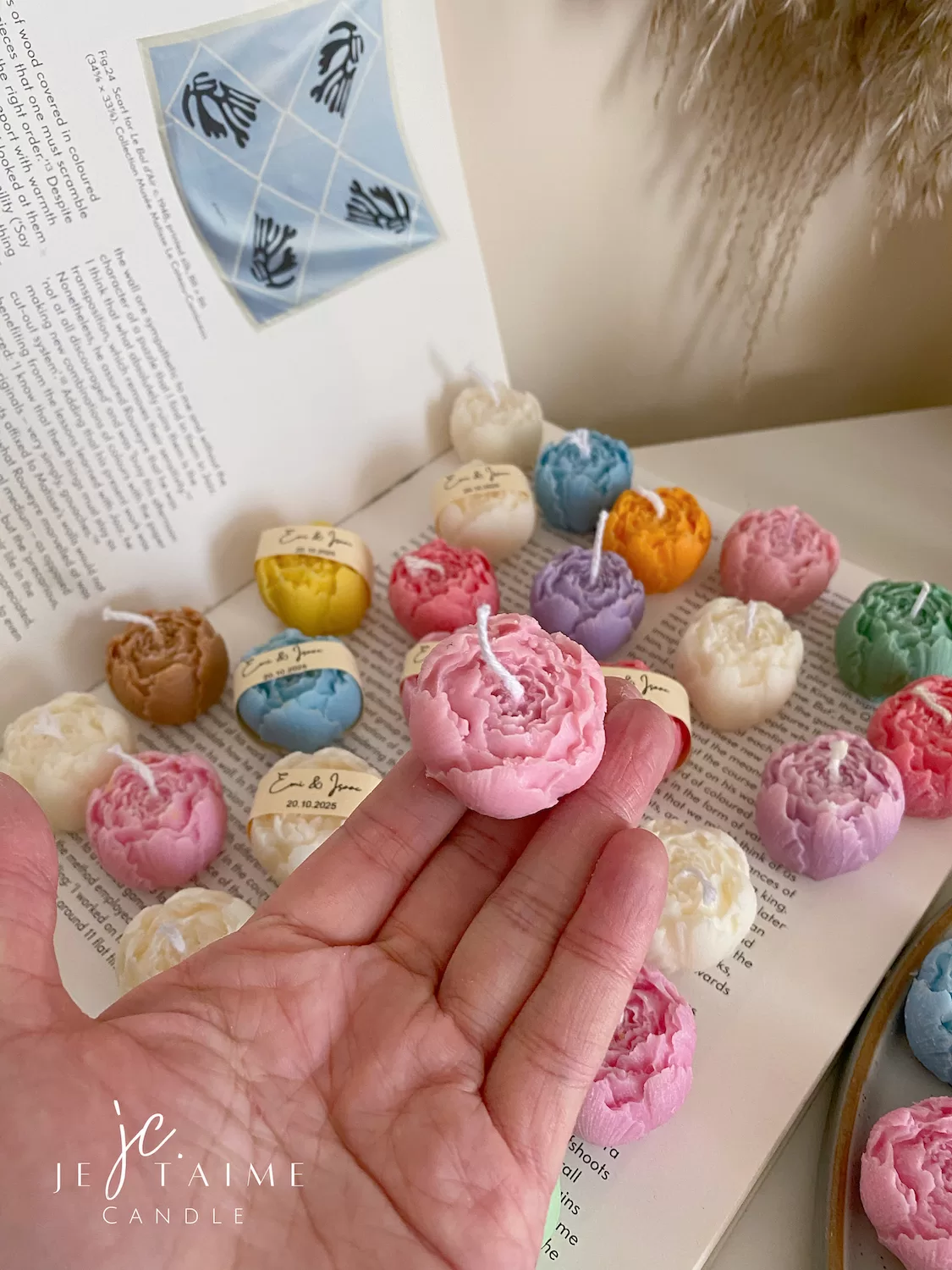 A book with an assortment of colorful candles on it, highlighting a Mini Peony Bud Candle, perfect for gifting at special events.