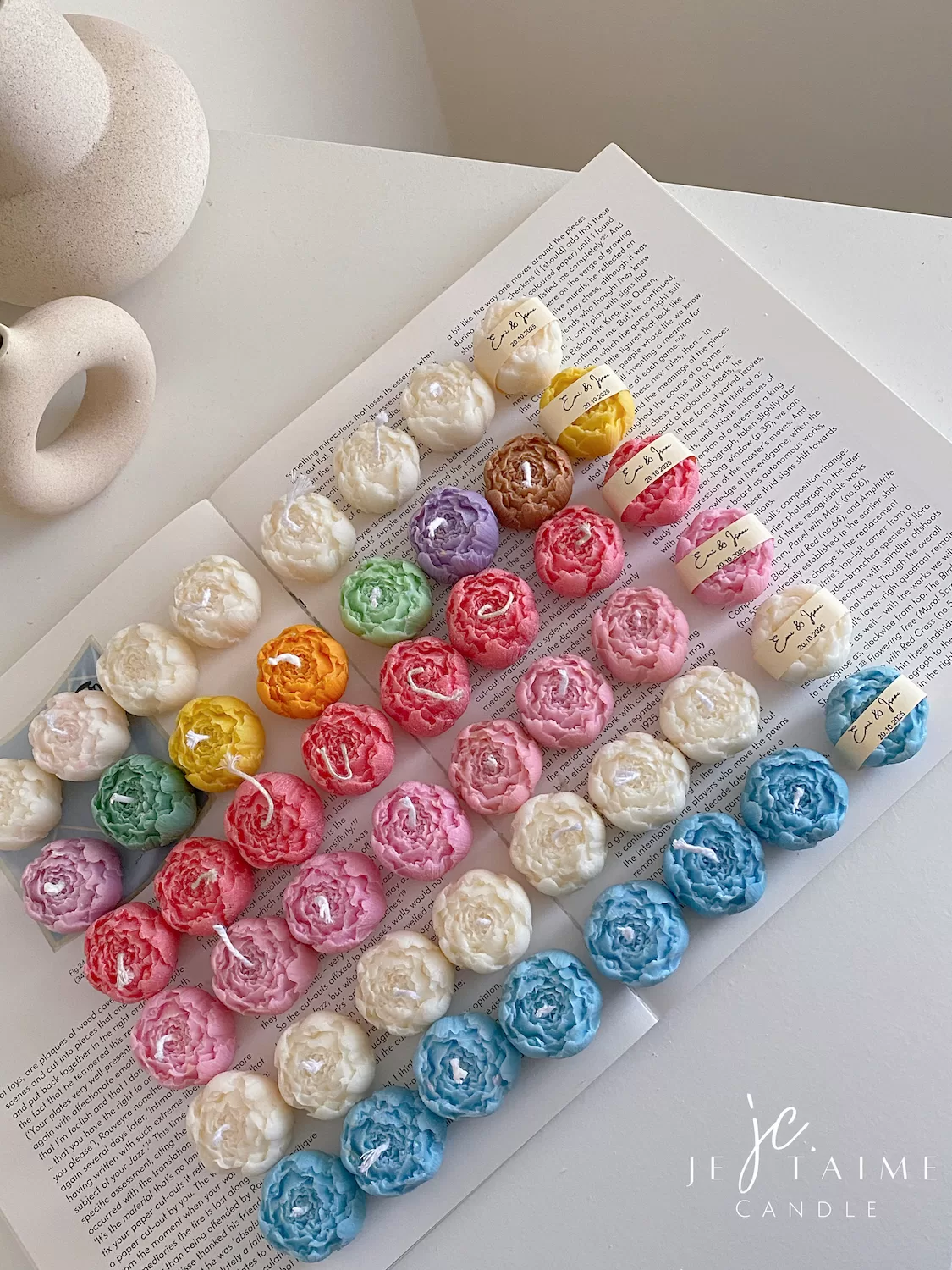 A book with an assortment of colorful candles on it, highlighting a Mini Peony Bud Candle, perfect for gifting at special events.
