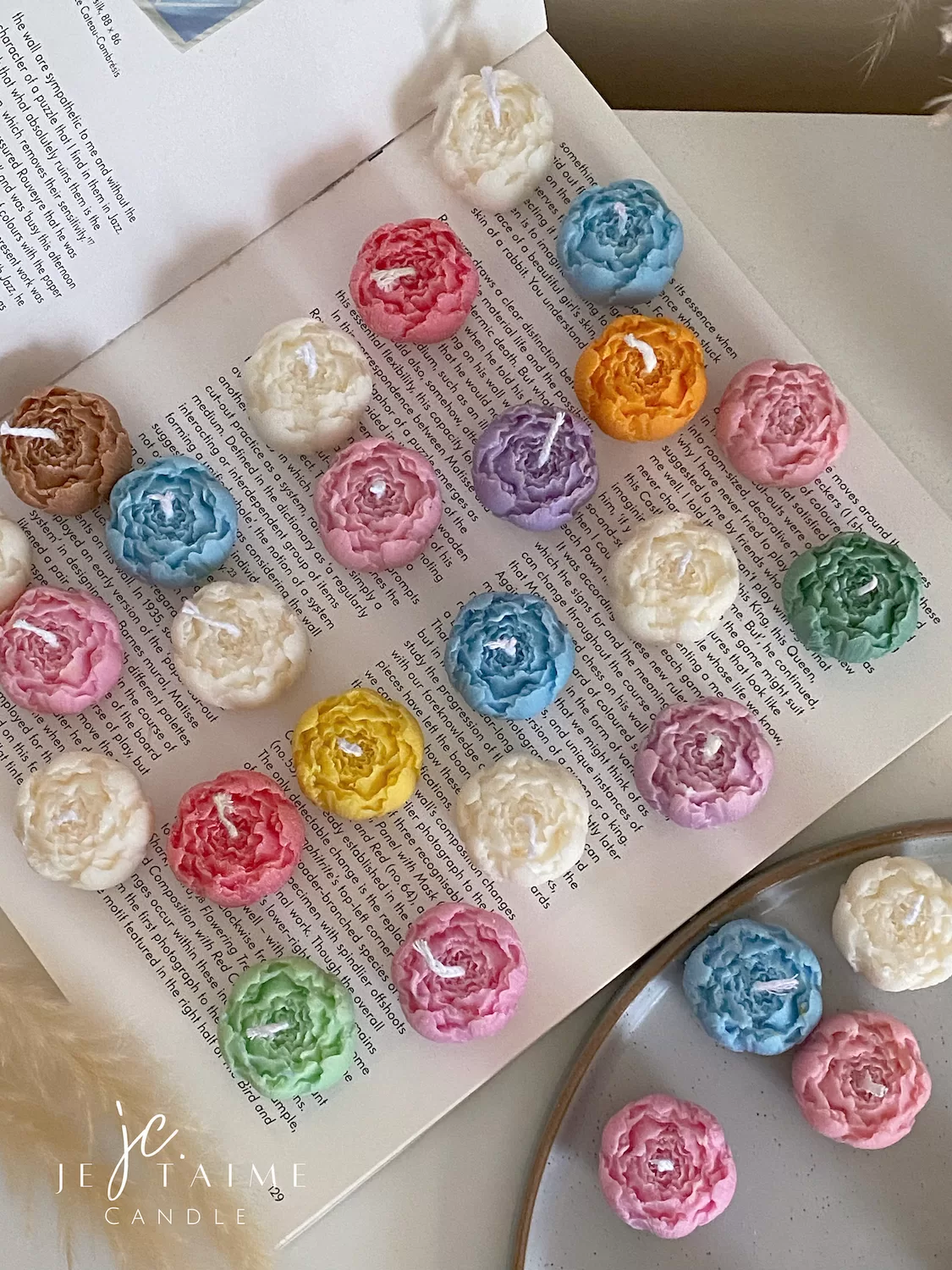 A book with an assortment of colorful candles on it, highlighting a Mini Peony Bud Candle, perfect for gifting at special events.