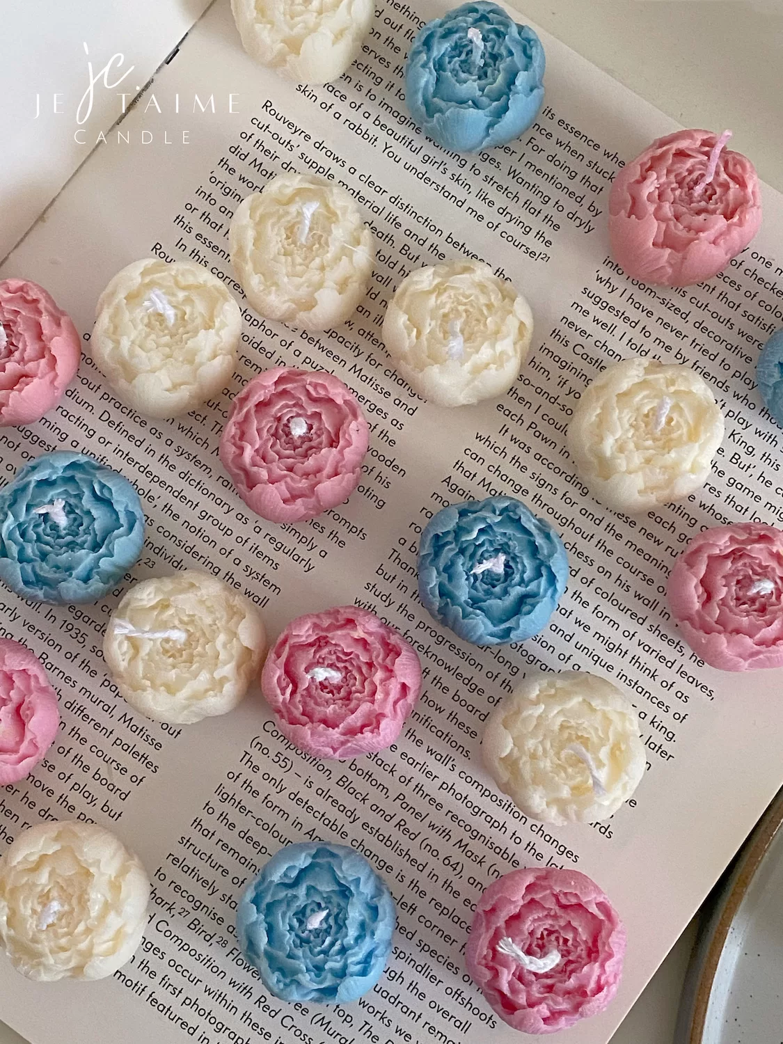 A book with an assortment of colorful candles on it, highlighting a Mini Peony Bud Candle, perfect for gifting at special events.