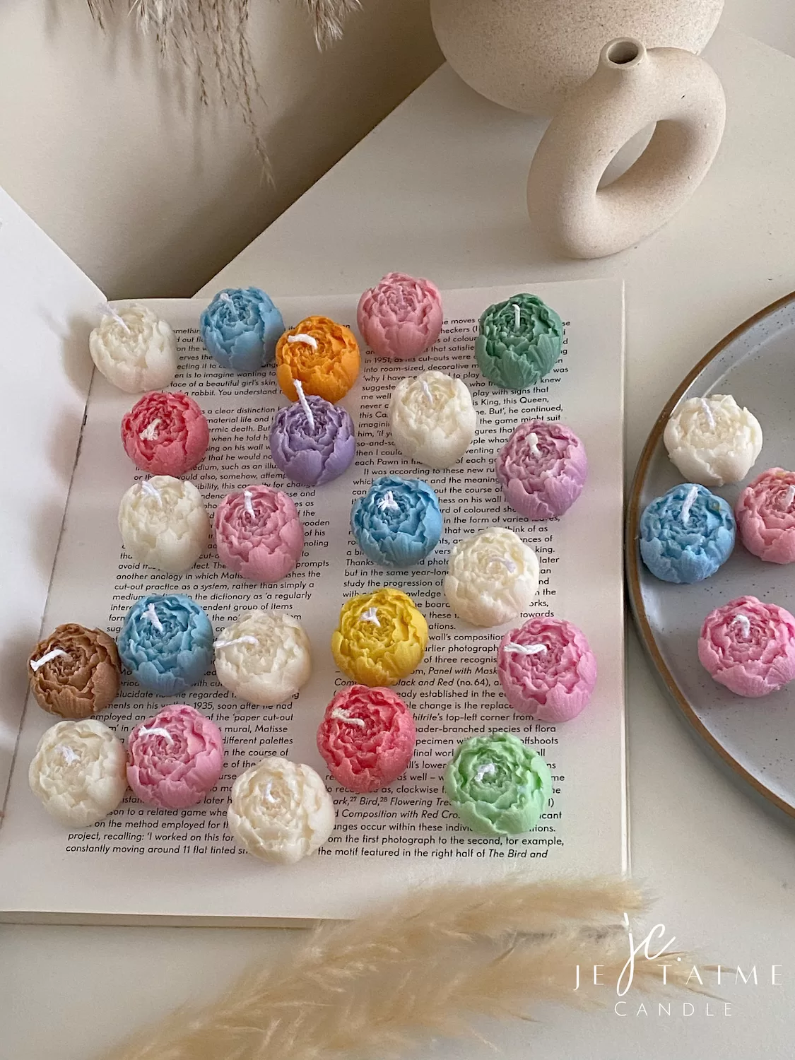 A book with an assortment of colorful candles on it, highlighting a Mini Peony Bud Candle, perfect for gifting at special events.