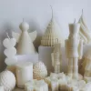 ollection of handmade decorative candles in Christmas shapes including houses, nutcrackers, snowflakes, pine cones, and Christmas trees, displayed on soft fabric with a pink ribbon.
