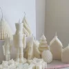 ollection of handmade decorative candles in Christmas shapes including houses, nutcrackers, snowflakes, pine cones, and Christmas trees, displayed on soft fabric with a pink ribbon.