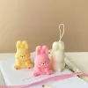 Three cute chubby bunny-shaped candles in pastel colors—yellow, pink, and white—sitting on a white surface with pink ribbon and wooden matches. Each bunny candle features detailed facial expressions, rosy cheeks, and tiny paw prints with heart designs. These kawaii bunny candles are perfect for Easter décor, baby showers, birthday gifts, or cozy home decoration.