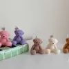It looks like the image shows five teddy bear–shaped candles in different colors (purple, pink, light brown, cream, and medium brown) sitting in a row on a white surface. Each candle has a wick on top with a small tag that says 