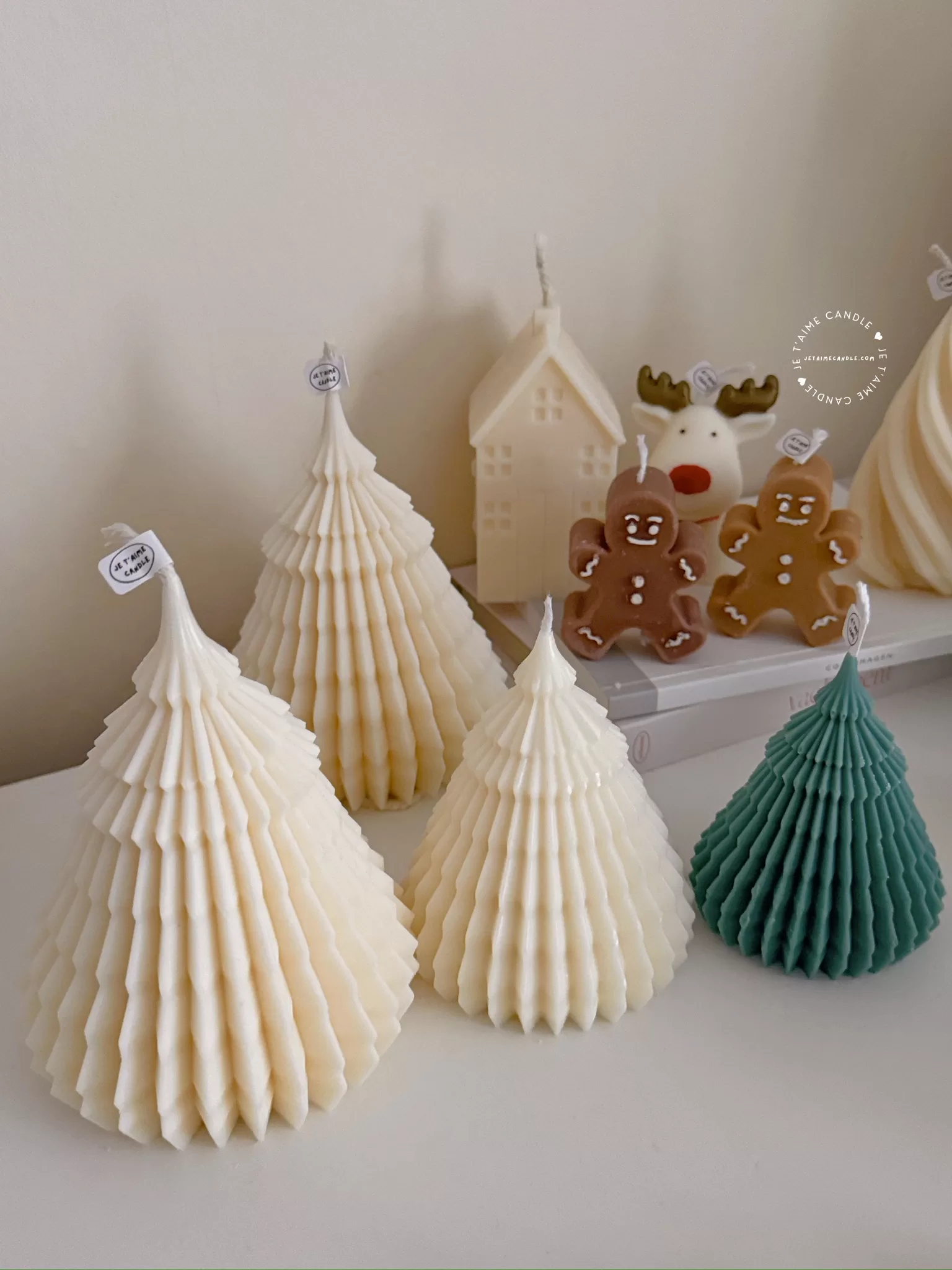 Four tree-shaped candles in cream and green colors are displayed in the foreground, with house, reindeer, and gingerbread man candles in the background.