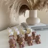 Handmade teddy bear candles in brown and cream colors, decorated with festive collars and golden bells, labeled 