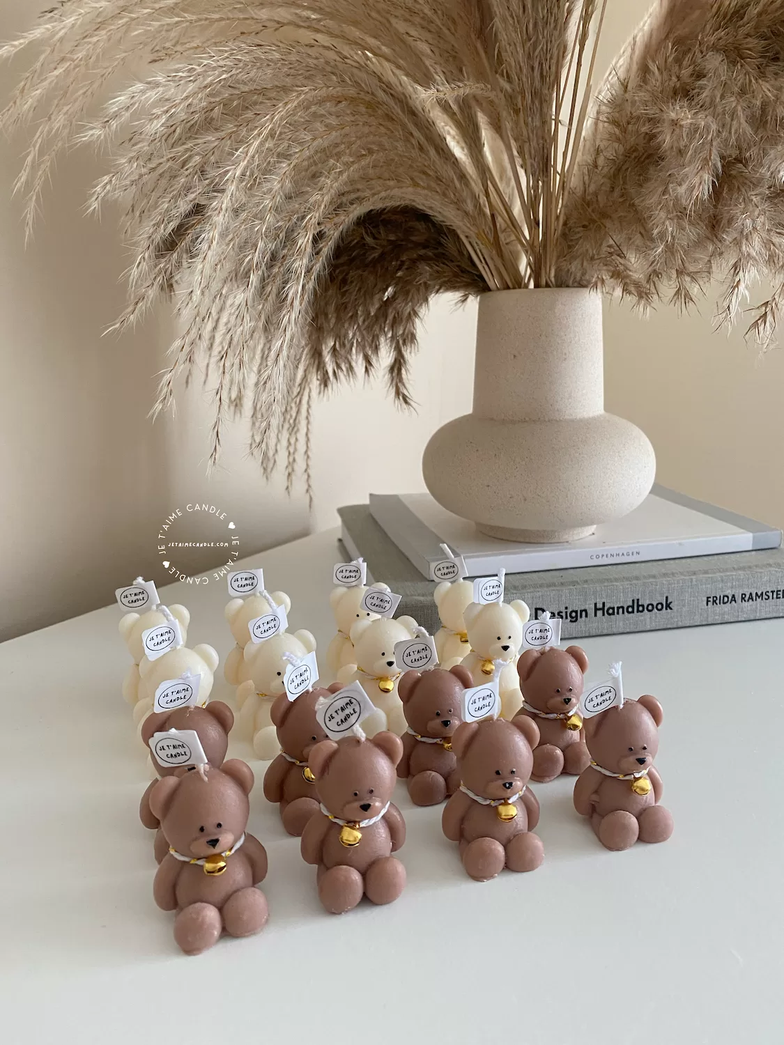 Handmade teddy bear candles in brown and cream colors, decorated with festive collars and golden bells, labeled "JE T’AIME CANDLE" – perfect for gifts, parties, and home decor