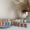 Handmade teddy bear candles in brown and cream colors, decorated with festive collars and golden bells, labeled 