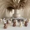 Handmade teddy bear candles in brown and cream colors, decorated with festive collars and golden bells, labeled 