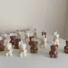 Handmade teddy bear candles in brown and cream colors, decorated with festive collars and golden bells, labeled 